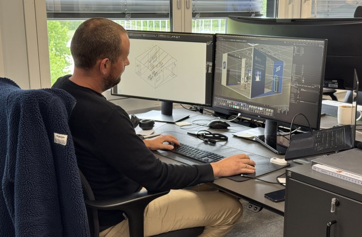 En mann i mørk genser sitter ved dataskjerm og jobber med tredimensjonale modeller. Han er på et kontor.