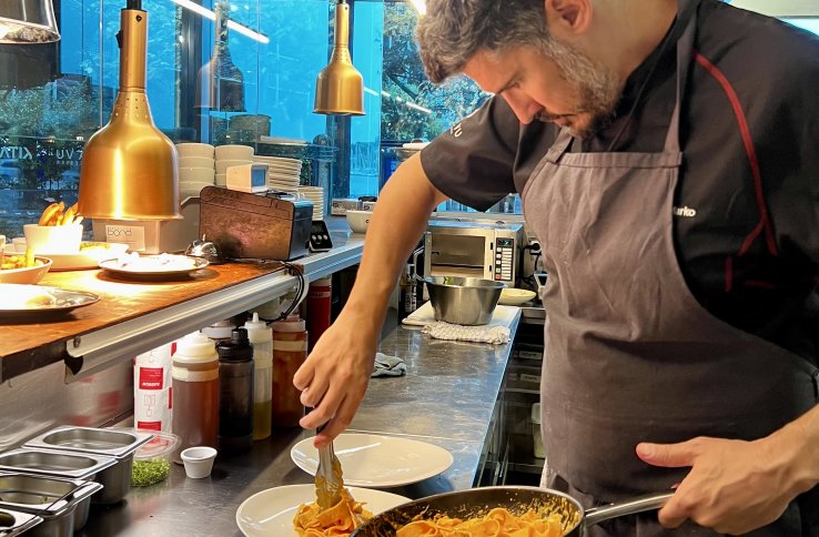 Mann i med skjegg i svarte kokkeklær legger opp pasta på en tallerken