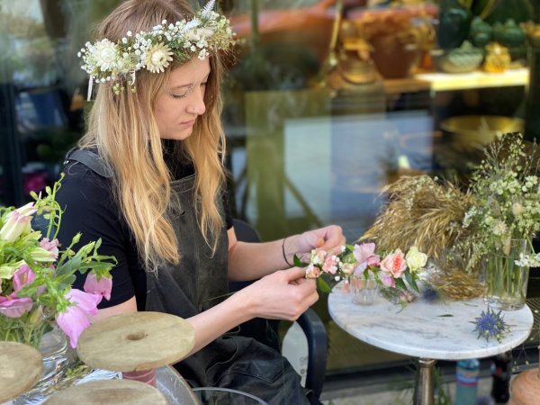 Blomsterdekoratør Ingrid Marie Aarre med blomsterkrans i håret lager en blomsterkrans med rosa blomster