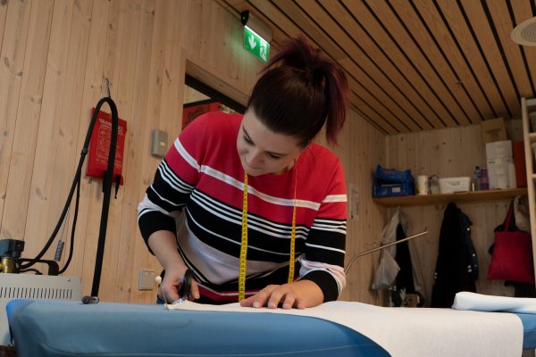 Bunadstilvirker Julia Wach klipper på et stykke tøy som ligger på et bord.