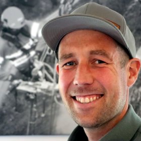 Smilende ung mann med grå caps og grå skjorte.