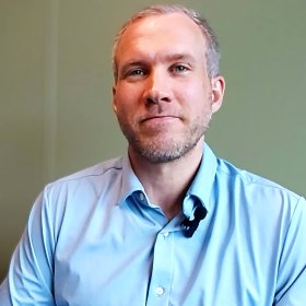 Leder Sebastian Hennig En mann i et lyseblå skjorte. Han smiler og ser rett i kameraet.