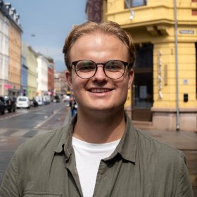 En mann i et grønn skjorte. Han smiler og ser rett i kameraet. 