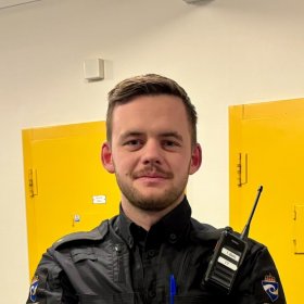 En mann med skjegg og svart uniformsjakke står foran to gule dører