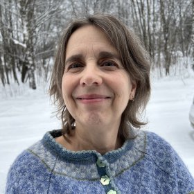 Portrettbilde av en dame med mørkt hår og lyseblå ullgenser. Snø i bakgrunnen