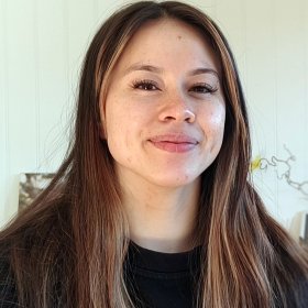En kvinne med langt mørkt hår. Hun har på seg en svar overdel.