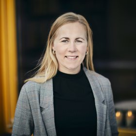 Advokat Marit Opsahl Jukvam En kvinne med langt blondt hår står ute foran et bygg med gule karmer. Hun smiler rett mot kamera. Hun har på seg en rutete blazer over en mørk genser.