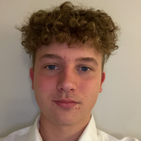 En mann i hvit trøye og blond hår står foran en hvit vegg