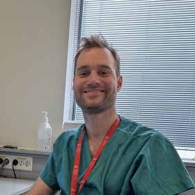 En mann med mørkt hår og skjegg og grønn skjorte sitter foran et vindu