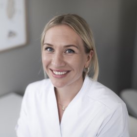 Ei dame med hestehale og hvit skjorte sitter foran en lys vegg