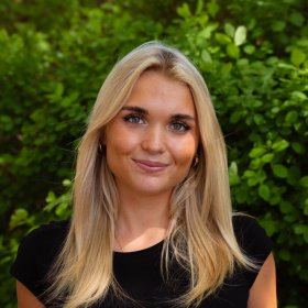 Dame med svart t-skjorte og lyst hår. Hun smiler og ser rett i kameraet.