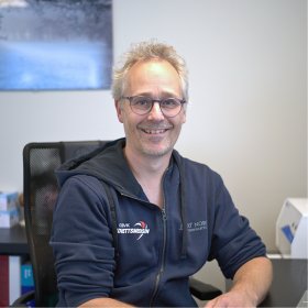 Mann i blå hettegenser smiler.