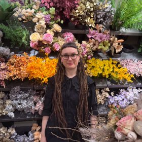 Kvinne med langt brunt hår, iført svart skjorte og briller, poserer foran kamera.