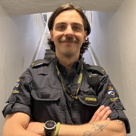 Jakob jobber i et spesielt tøft miljø i Oslo fengsel. En ung mann i uniform står nederst i en trapp. Han holder armene foldet foran brystet.