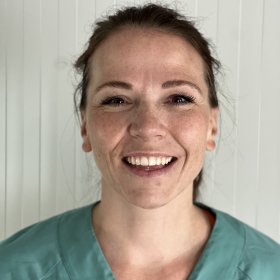 Kvinne med hestehale og grønn operasjonsuniform. Hun smiler og ser rett inn i kameraet.