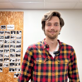 Portrettbilde av Animatør. Mann i rutete rød- og gulskjorte poserer foran kamera. I bakgrunnen skimtes en vegg med bilder fra kontorlandskapet.