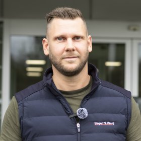 Mann i grønn skjorte og blå vest smiler og ser inn i kameraet. 