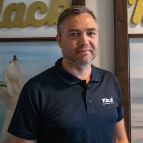 Markedssjef Ken Stian Olsen. Han har på seg blå t-skjorte. Han står foran et bilde med en isbjørn.