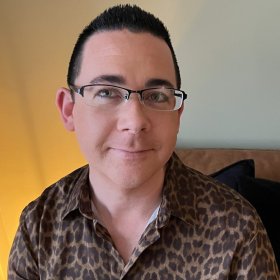 Kreftsykepleier Fredrik von Löwensprung Eiesland En mann med kort, mørkt hår og briller smiler rolig mot kamera. Han har på seg en brun skjorte med leopardmønster og sitter foran en lys gul vegg.