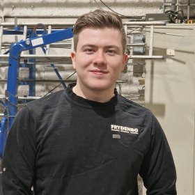 Mann med svart genser står i et verktsted og ser inn i kamera