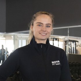 En kvinne i treningstøy. Hun smiler. Hun er på et treningssenter. 