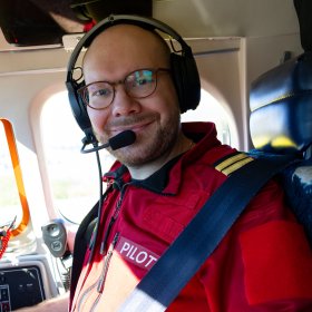 En mann i rød pilot-uniform. Han er i et fly.