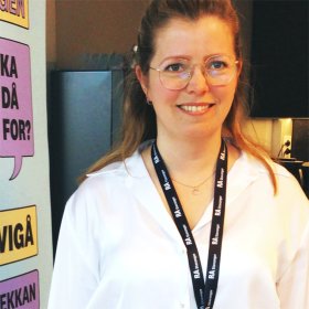 En dame med langt hår og hvit bluse. Hun ser rett i kameraet og smiler.