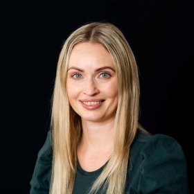 Smilende kvinne med blå øyne og langt lyst hår delt i midtskill.