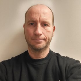 Mann med svart genser ser inn i kamera. Hvit bakgrunn. 