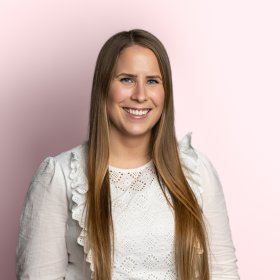 Portrettbilde av en dame med langt, mørkeblond hår og hvit topp. Bakgrunnen er lys rosa