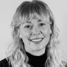 Et svart-hvitt portrettbilde av en jente med langt hår og som smiler til kamera