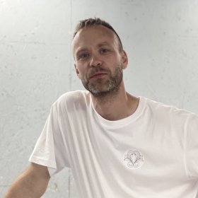 En mann i hvit t-skjort står foran en hvit vegg
