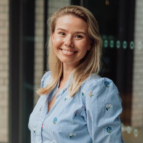 Dame med lyst hår og lyseblå skjorte smiler til kamera