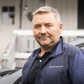 Mann i mørk vest og blå skjorte. Han ser rett i kameraet. Han er ute.