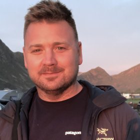 Mann med svart genser og jakke og brunt hår ser inn i kamera