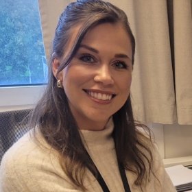 Flygeleder Martine Rødseth Hjørungdal Dame med brunt hår, hvit genser og et nøkkelkort rundt halsen smiler inn i kamera