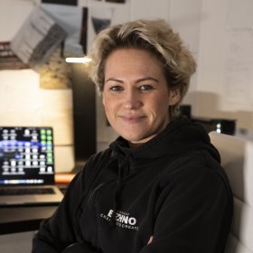 En dame med blondt hår og svart genser. Hun ser rett i kameraet.