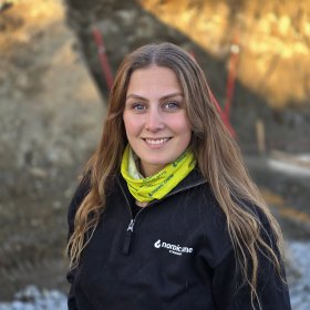 Kranfører Dorthe Sandvik Dame med lysebrunt hår løst, gul buff og svart jakke ser inn i kamera og smiler.