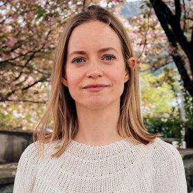 Forsker Mari Fjalstad Jensen Dame med lys genser står foran kirsebærtrær, hun ser inn i kamera.