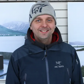 En mann i mørke klær. Han smiler og ser rett i kameraet. 