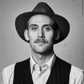 Anders Brunvær Hauge er en mann på 38 år med bart, bredbremmet hatt, lys skjorte og svart vest.