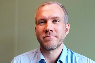 Leder Sebastian Hennig En mann i et lyseblå skjorte. Han smiler og ser rett i kameraet.