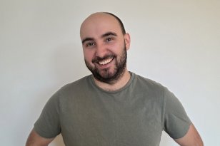 Portrettfoto av skoleassistent Tommy Egeland Mann med mørkt, kort skjegg og en grønn t-skjorte står foran en lys vegg og smiler til kamera.