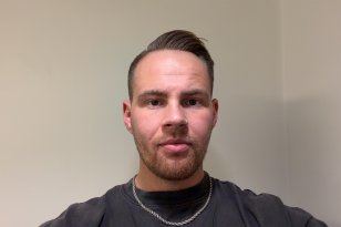 En mørkhåret mann med brune øyne og piercing i nesen ser inn i kamera