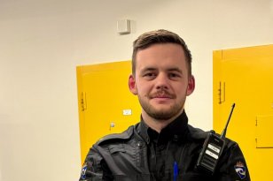 En mann med skjegg og svart uniformsjakke står foran to gule dører