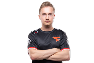 En ung mann står med armene i kors mot en hvit bakgrunn. Han har kort, lyst hår og et nøytralt ansiktsuttrykk. Han har på seg en svart e-sportdrakt med røde detaljer og en tydelig laglogo på brystet.