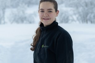 Ei dame i mørkeblå genser. Hun smiler til kameraet. Hun er ute. Det er snø bak henne.