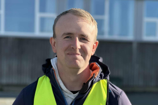 Barne- og ungdomsarbeider Einar Johansen  Mann med blå jakke og gul refleksvest står foran en bygning med vinduer