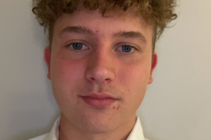 En mann i hvit trøye og blond hår står foran en hvit vegg