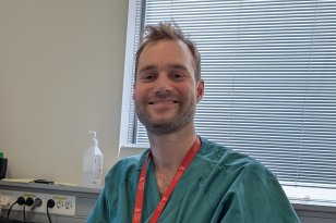 En mann med mørkt hår og skjegg og grønn skjorte sitter foran et vindu